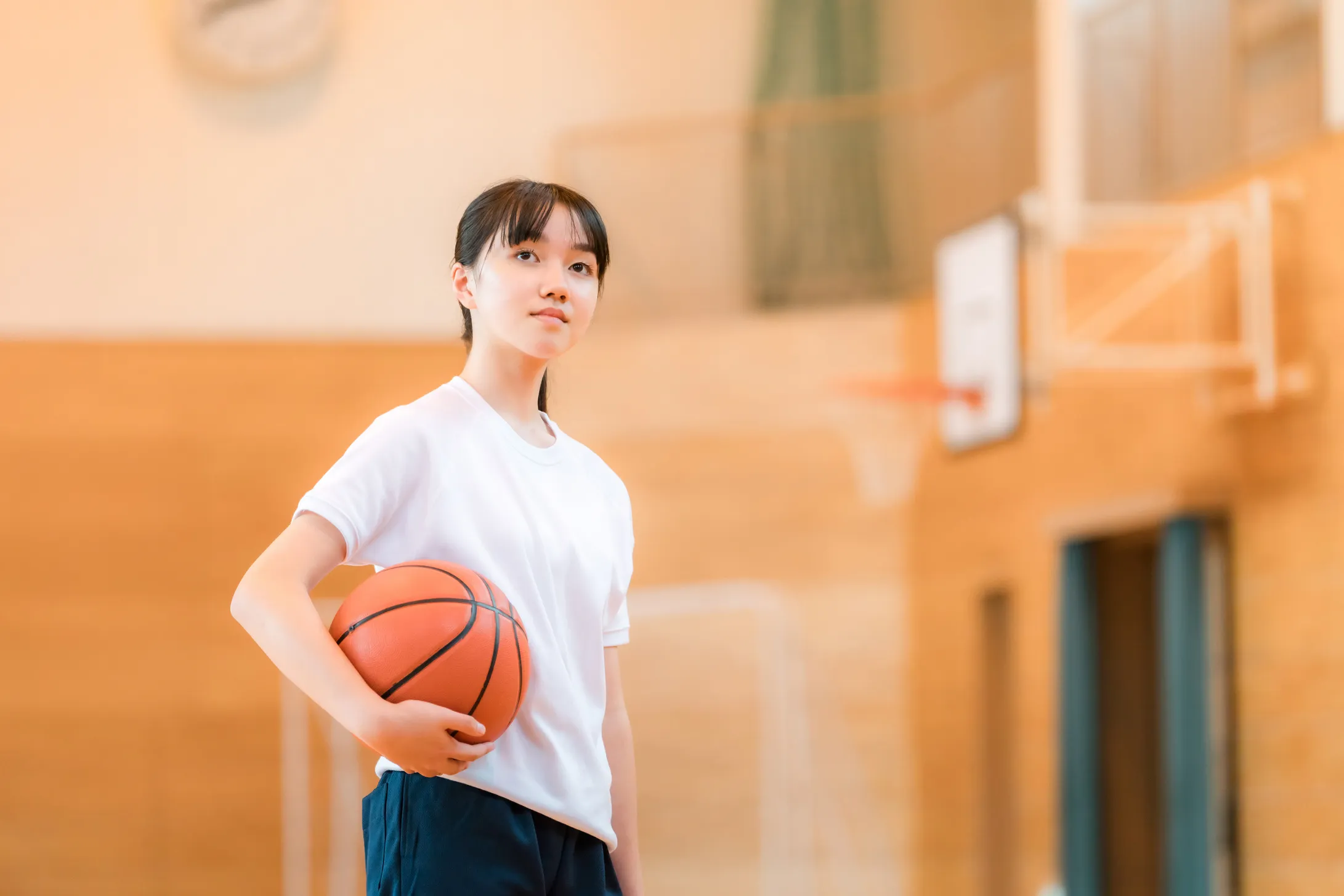 体育館でバスケットボールを抱えて立つ女の子