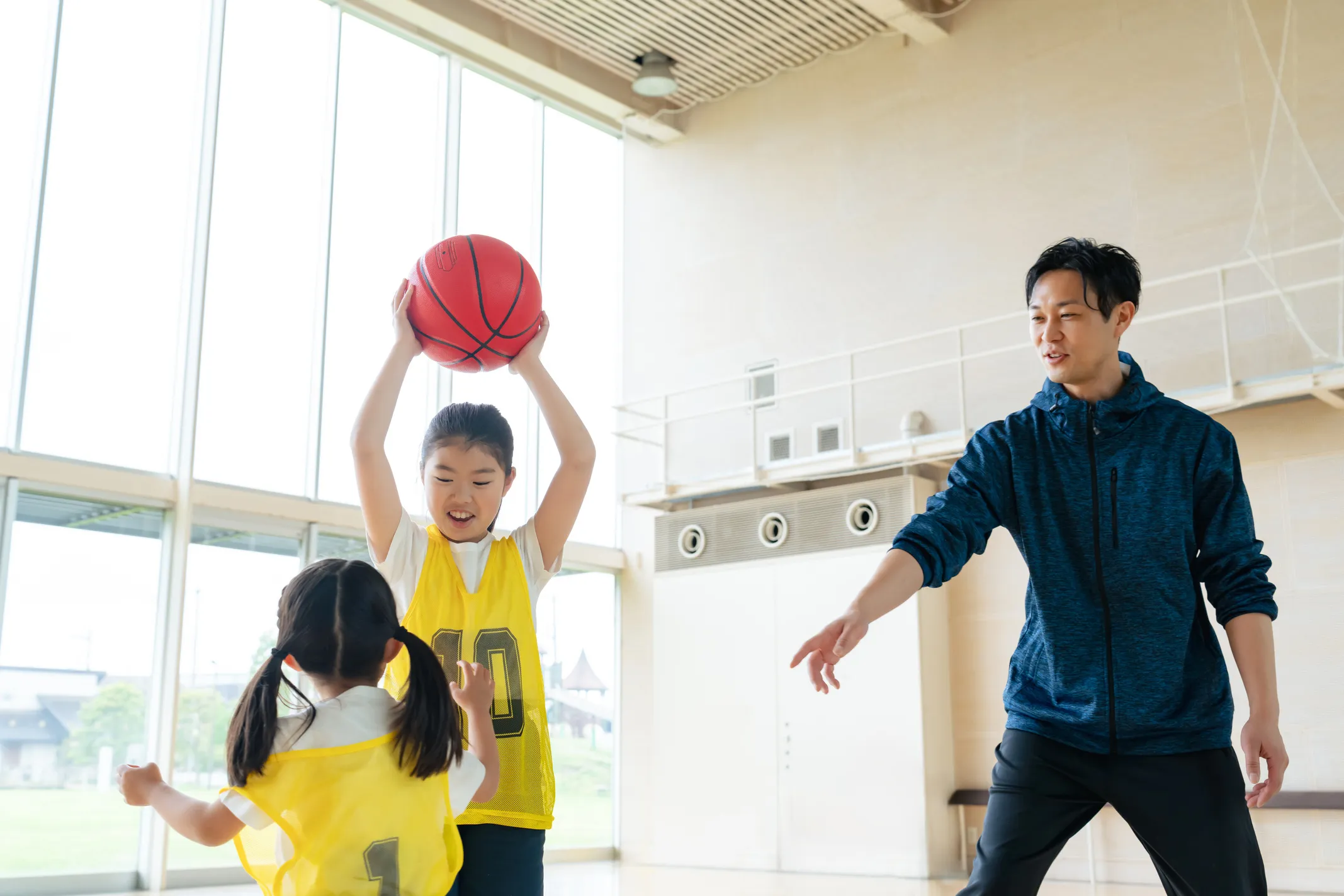 体育館で子どもたちがバスケットボールの練習をしコーチが指導している様子